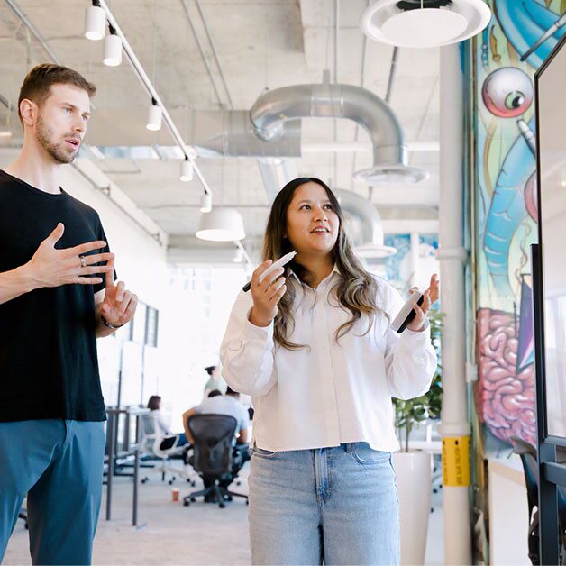Two people looking and gesturing at a white board